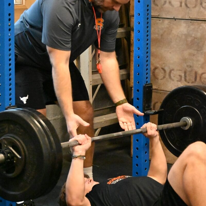 Teenager lifting weights while coach assisting